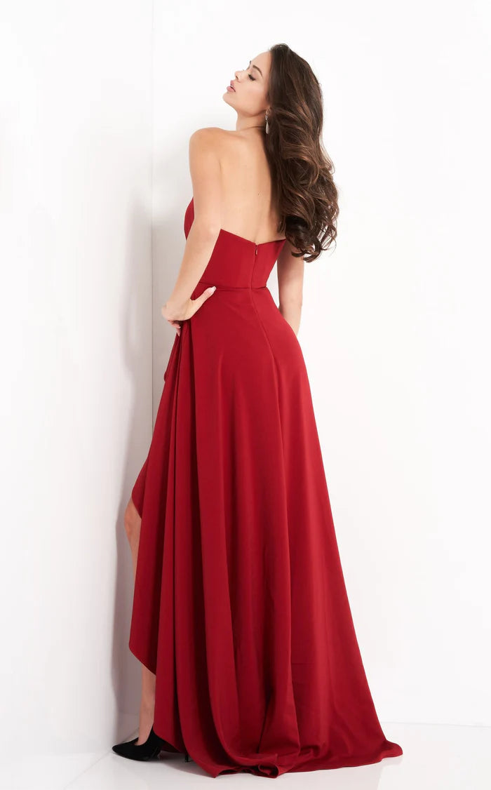 Elegant burgundy strapless gown by Jovani, featuring a jeweled waist accent and a high side slit, styled for a formal evening event.