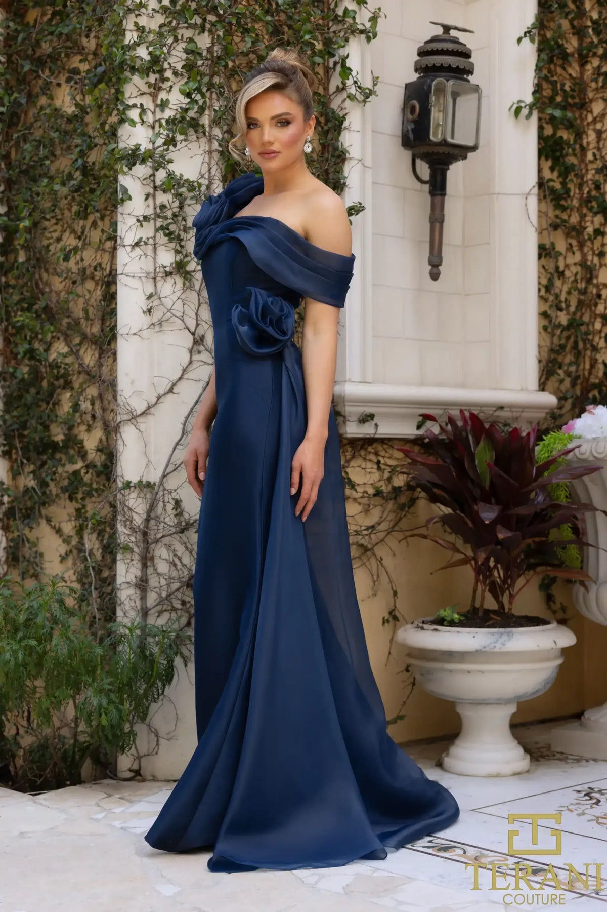 Terani Couture 242M3342 Asymmetric Off-Shoulder Gown with rose detailing, available in navy and emerald. Perfect for formal evening events and Mother of the Bride or Groom.