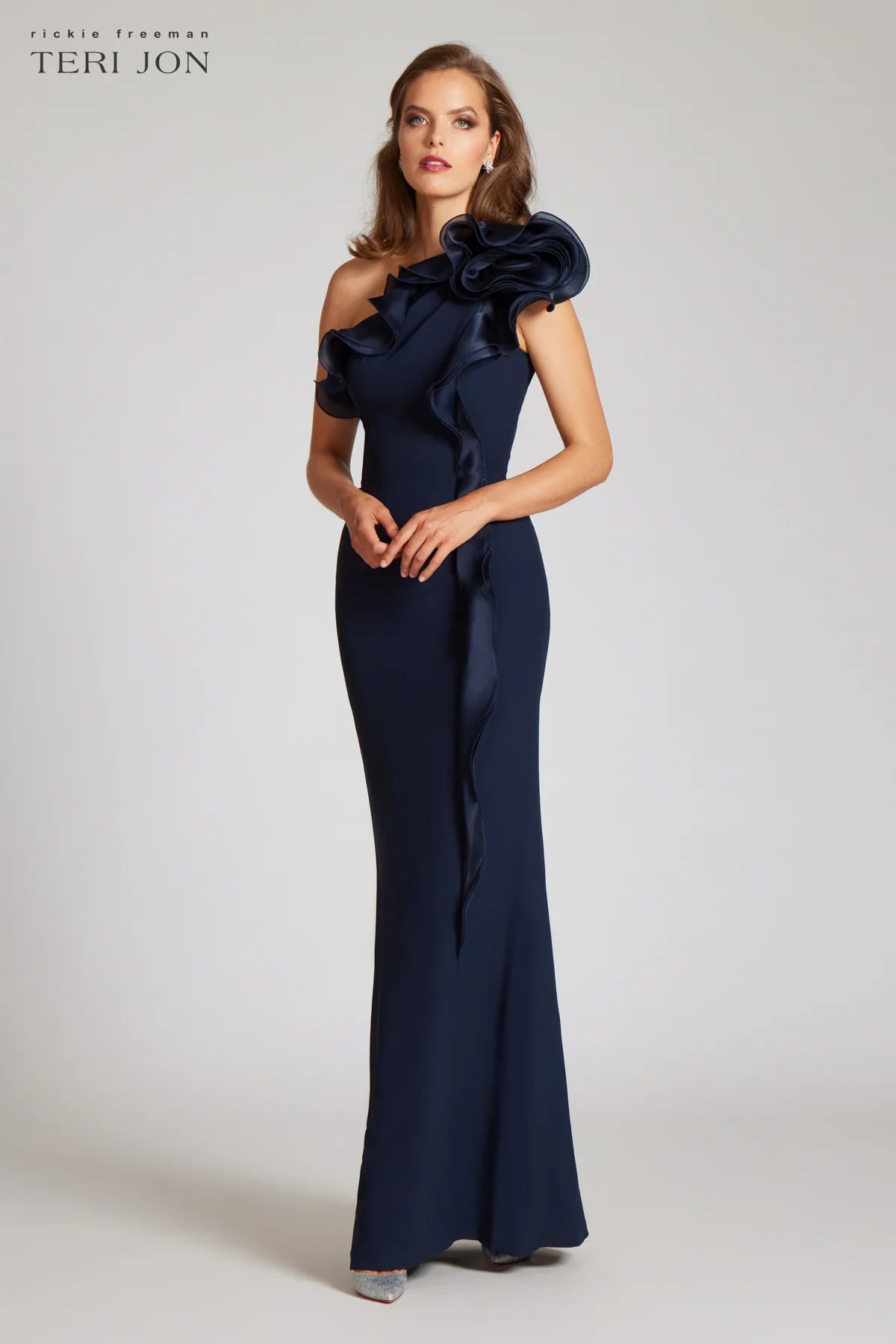 Teri Jon 249043 one-shoulder gown featuring a cascading ruffle detail and fitted silhouette. Perfect for formal evenings and mother of the bride or groom.  Model is wearing the dress in the color navy.